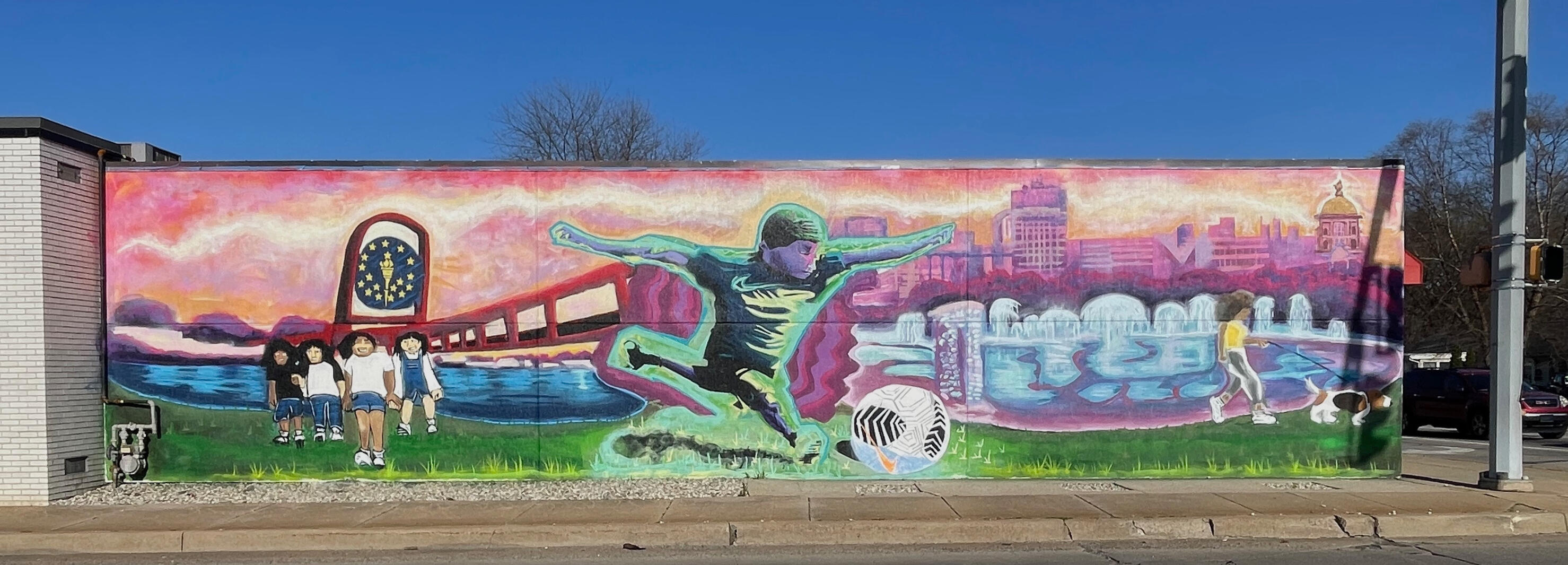 Large-scale exterior community public art mural featuring local youth, the Indiana state torch, and the South Bend skyline hand-painted for Kings Play Place by VanGalder Murals