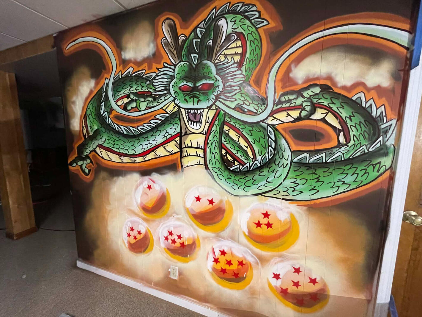 Custom hand-painted residential interior mural featuring the massive green eternal dragon Shenron and the seven glowing Dragon Balls from Dragon Ball Z, executed on a paneled wall for a private man cave by VanGalder Murals
